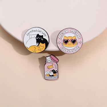 Three vibrant Cat Lady Brooch pins from KittyNook Cat Co., including “Meow Meow Catitude” and “Antidepressants” jar.